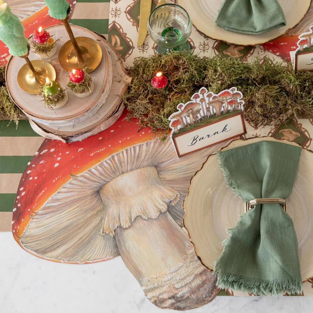 Decorative table setting with a large mushroom plate, green napkin, and candles on a patterned tablecloth.