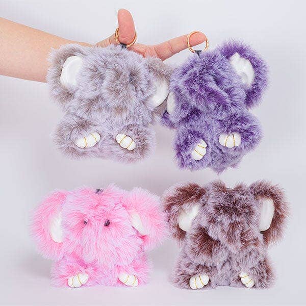 Four plush elephant-shaped keychains or phone cases in light gray, purple, pink, and brown, shown with a hand holding two of them against a plain light background.