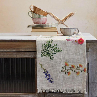 Table setting with floral tablecloth, cups, and books on a wooden surface.