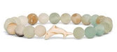A beaded bracelet made of round, polished stone beads in soft pastel shades of green, beige, and cream, with a small carved light wood dolphin charm at the center, shown on a plain white background.