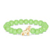 A beaded stretch bracelet featuring light green round beads and a small carved cream-colored dog charm in the center, displayed on a clean white background.