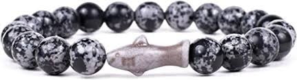 A beaded stretch bracelet featuring round black and white speckled stone beads with a central metallic silver fish charm, shown against a plain white background.