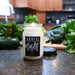 Candle labeled 'Farmers Market' on a kitchen counter with produce in the background