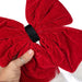Red velvet bow with a hand adjusting it on a white background