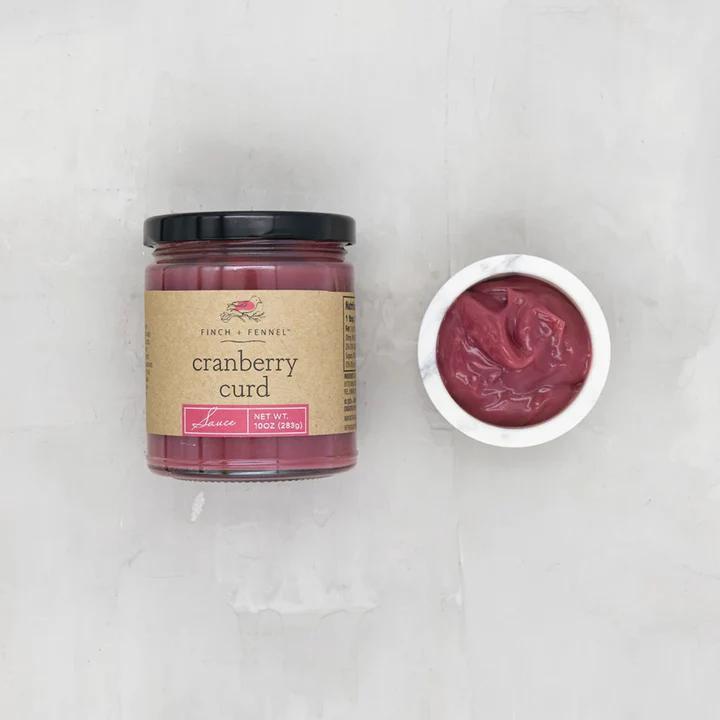 Jar of cranberry curd with a small dish of curd on a light gray background