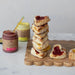 Stack of heart-shaped pastries with jam on a wooden board, accompanied by jars of cranberry curd.