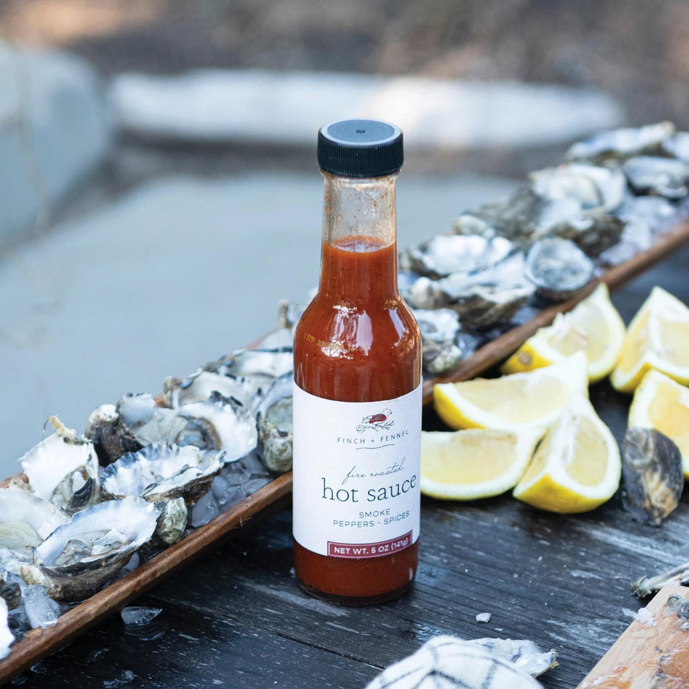 Bottle of hot sauce on a wooden board with oysters and lemons outdoors