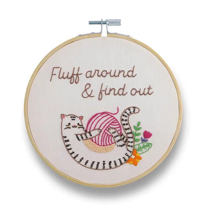 Embroidery hoop with a cat and yarn design and text 'Fluff around & find out' on a white background