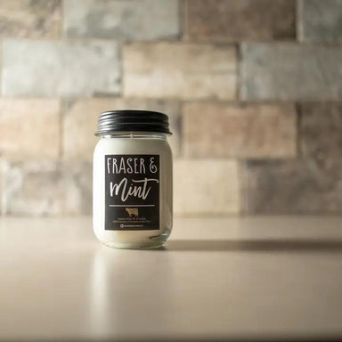 Candle in a mason jar labeled 'Fraser & Mint' on a countertop with a tiled wall background.