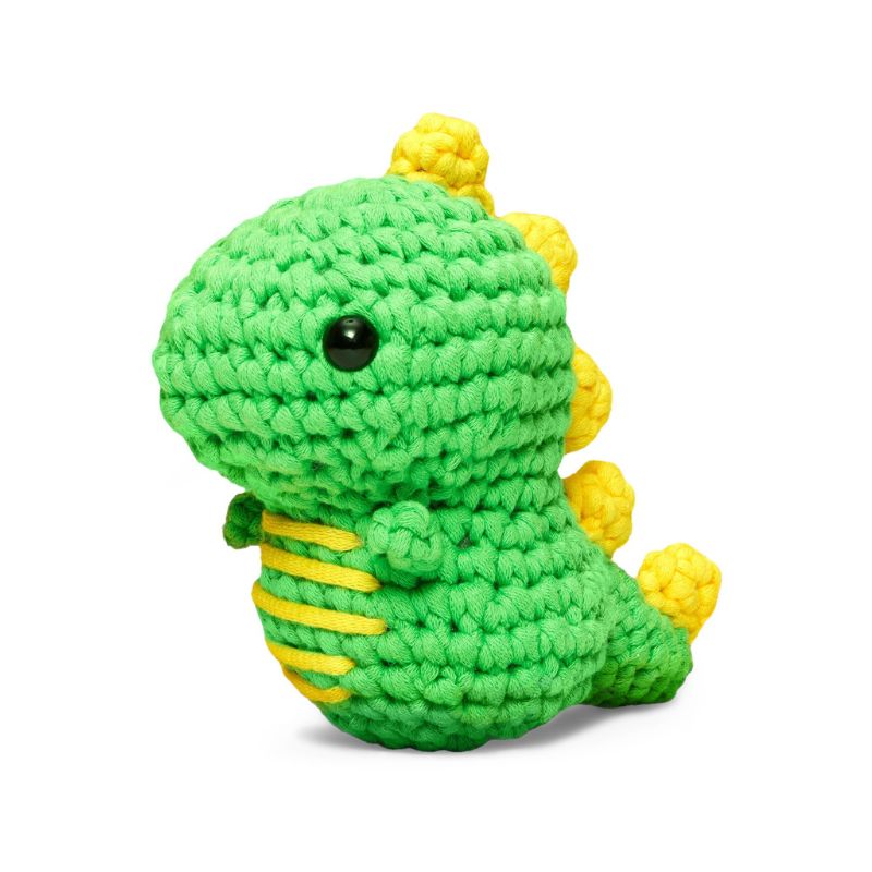 A green crocheted dinosaur plush toy with yellow spikes and a black bead eye, photographed on a clean white background.