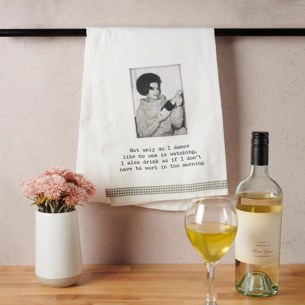 Towel with a printed design and text, wine bottle, glass, and flowers on a wooden surface.