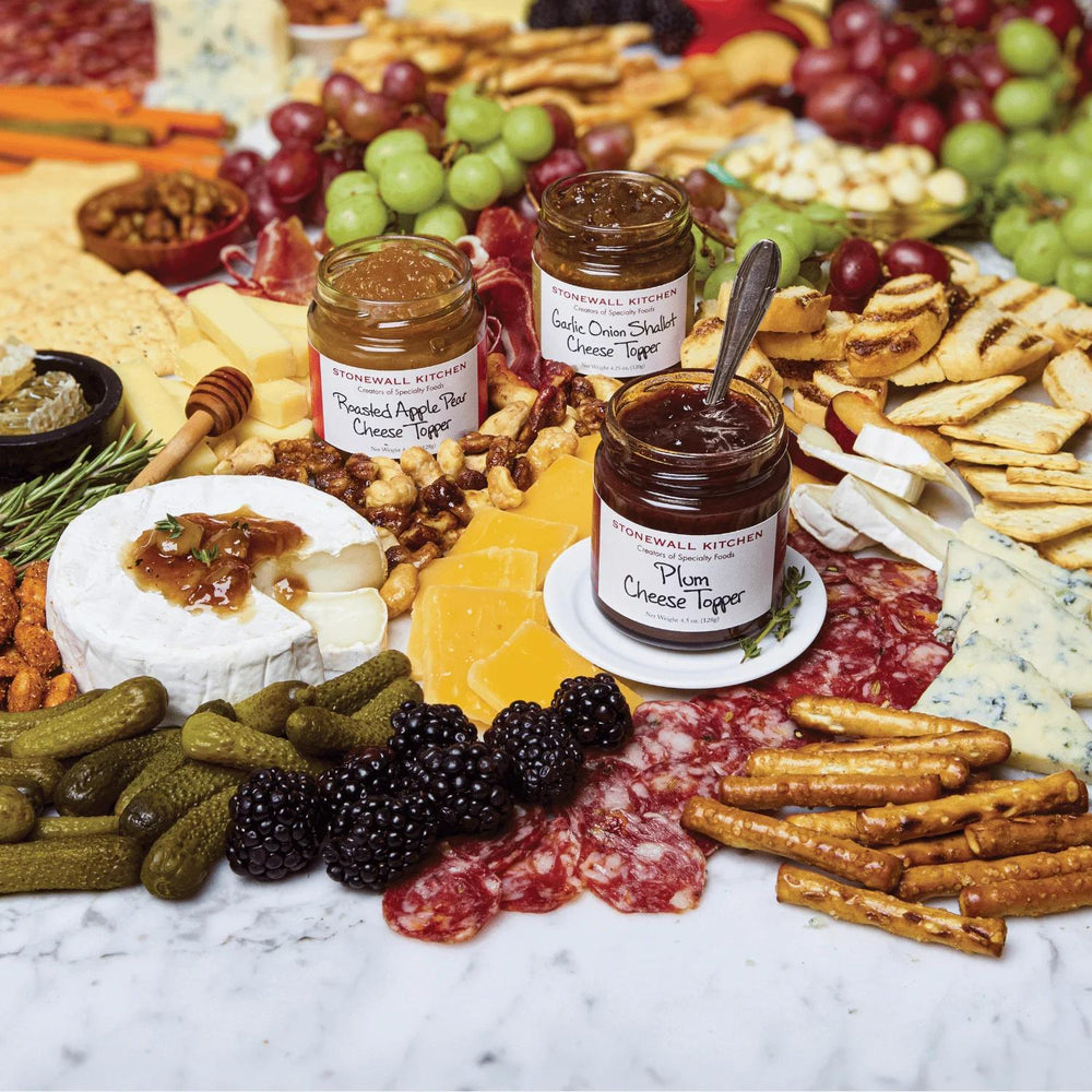 Assorted cheeses, fruits, and crackers with Stilton's Kitchen honey on a marble surface.