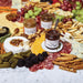 Assorted cheeses, fruits, and crackers with Stilton's Kitchen honey on a marble surface.