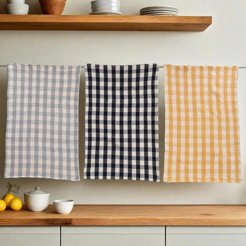 Three checkered towels in gray, black, and yellow hanging on a rack with a kitchen setting in the background.