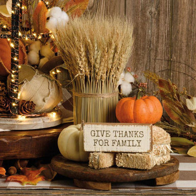 Decorative setup with pumpkins, wheat, and a sign saying 'Give Thanks for Family' on a wooden surface.