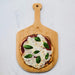 Small pizza with basil leaves on a wooden paddle with 'Kitch & Fennel' branding.