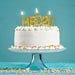 White cake with gold 'HBD2U' candles on a blue background