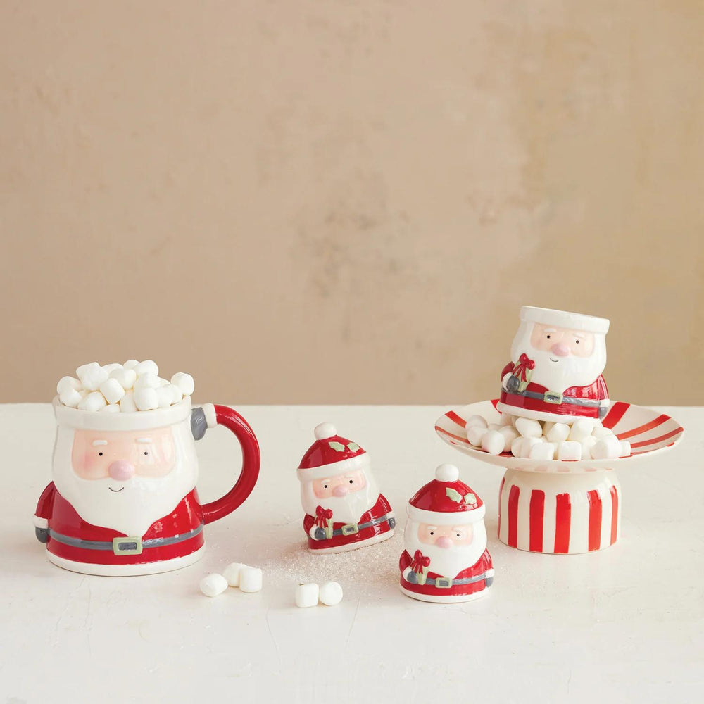 Set of Santa Claus-themed mugs and containers with marshmallows on a beige background