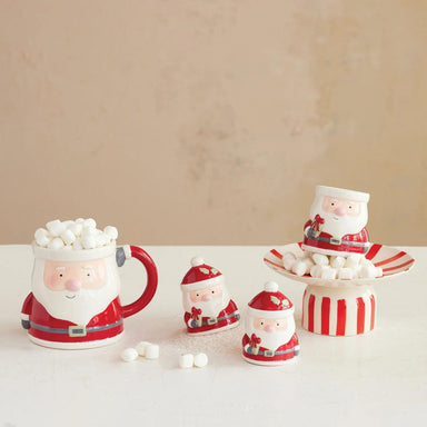 Set of Santa Claus-themed mugs and containers with marshmallows on a beige background