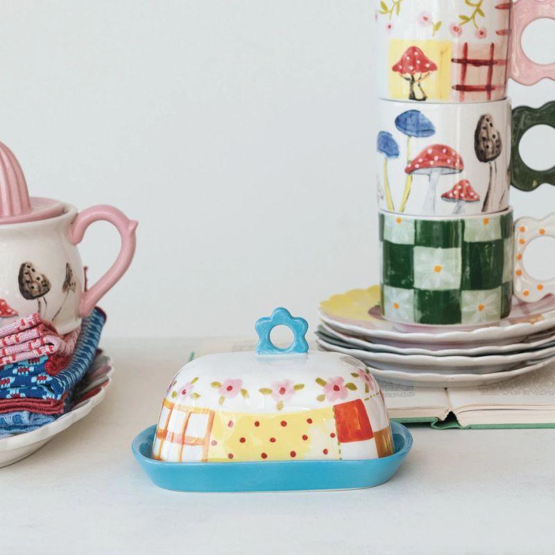Colorful ceramic items including a butter dish, cups, and saucers on a white surface.