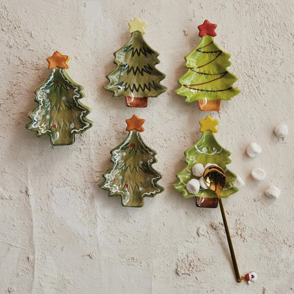 Set of four ceramic Christmas tree-shaped spoons on a textured white surface.