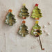 Set of four ceramic Christmas tree-shaped spoons on a textured white surface.
