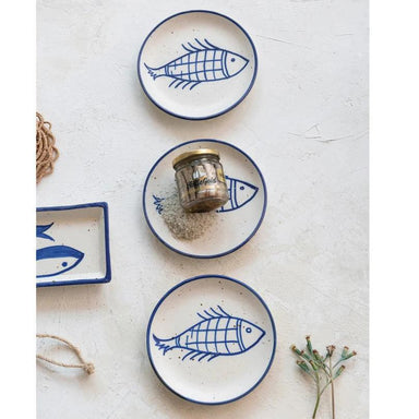 Set of ceramic plates with fish design on a textured white surface.