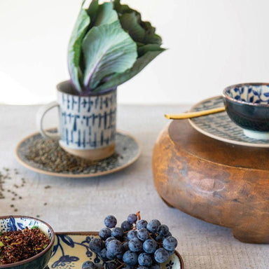 Ceramic cup with plant, wooden bowl, and grapes on a textured surface
