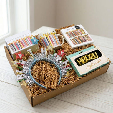Gift box with decorative items including a headband, mug, and cards on a light surface.