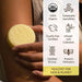 Hand holding a yellow bar of soap with certification icons on a white background