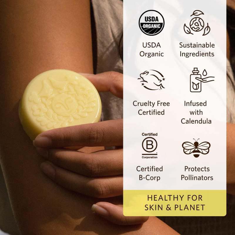 Hand holding a yellow bar of soap with certification icons on a white background