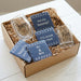 Two shot glasses with 'his' and 'hers' text, surrounded by blue cards in a box.