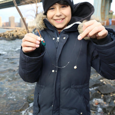 Child in a dark coat holding a fishing rod by a body of water