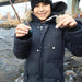 Child in a dark coat holding a fishing rod by a body of water