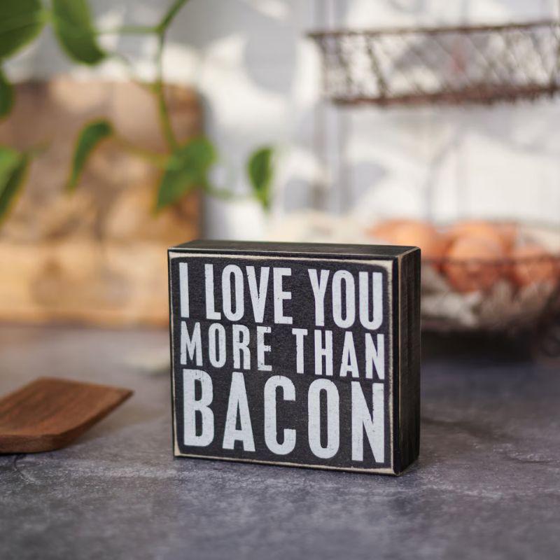 Small wooden block with 'I LOVE YOU MORE THAN BACON' text on a kitchen counter.