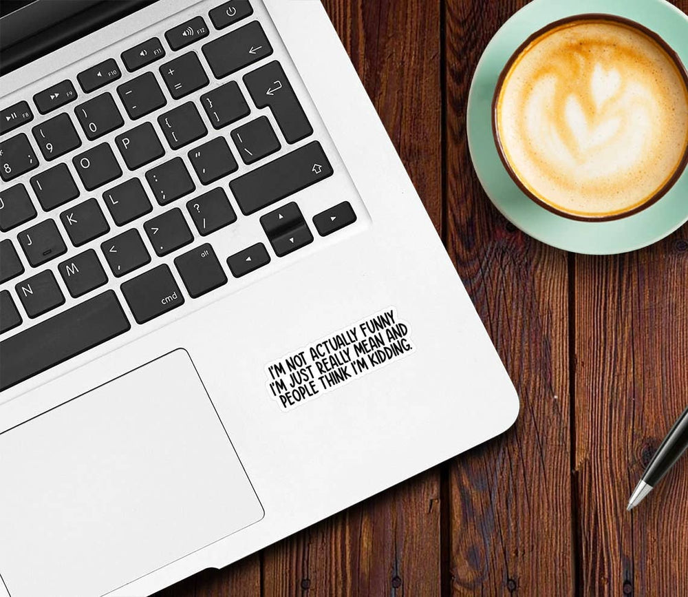 Laptop with humorous text on a wooden desk next to a cup of coffee.