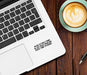 Laptop with humorous text on a wooden desk next to a cup of coffee.