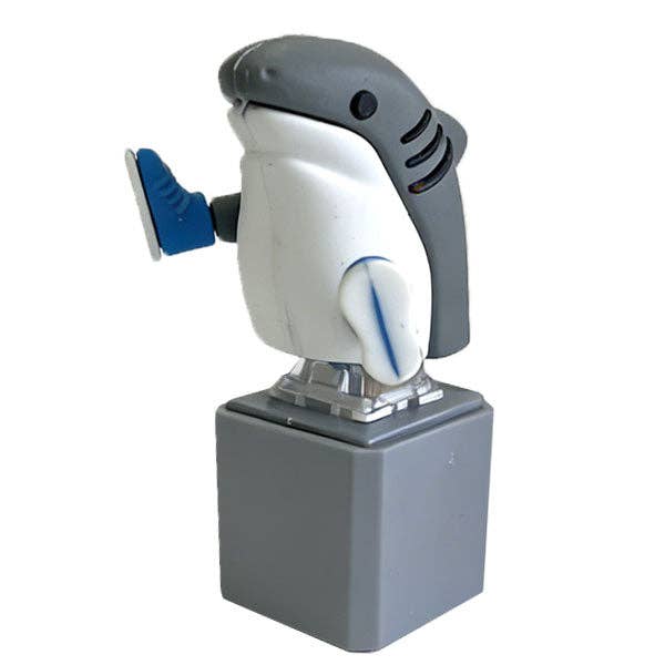 A shark-shaped novelty foot stuffer on a gray pedestal base, featuring a white and gray shark head with blue accents and a gray base, isolated on a white background.