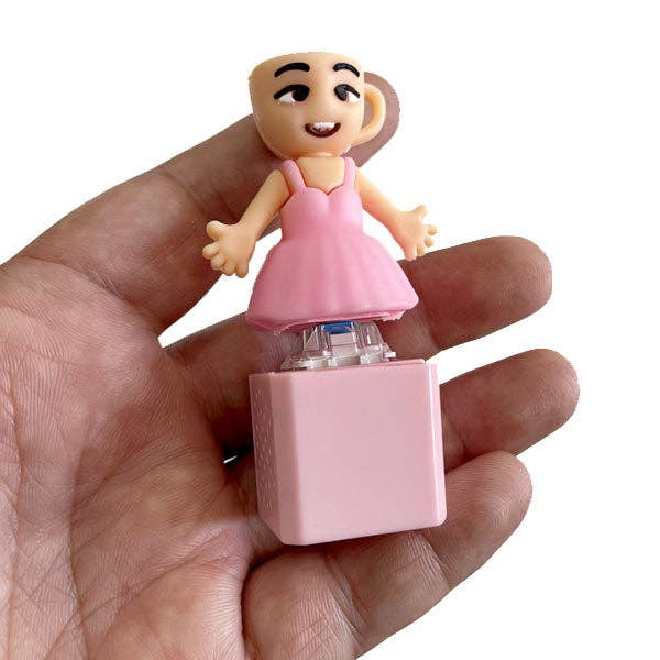 Small figurine of a character in a pink dress held in a hand against a white background