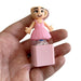 Small figurine of a character in a pink dress held in a hand against a white background