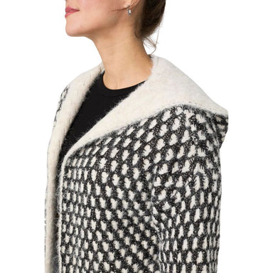 A close-up side view of a woman wearing a black and off-white textured knit cardigan with a fluffy cream sherpa collar over a black top, against a plain white background.