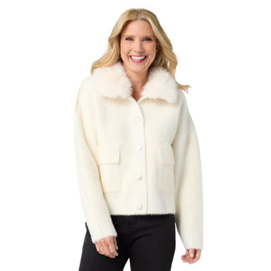 A smiling blonde woman wearing a cream-colored fuzzy cropped jacket with a fluffy collar and front buttons, paired with black pants, against a plain white background.