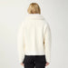 A model viewed from the back wearing a cream-colored fuzzy cropped jacket with a wide collar, paired with black pants, against a plain light background.