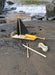 Toy sailboat with a black flag and yellow mast on a sandy beach.