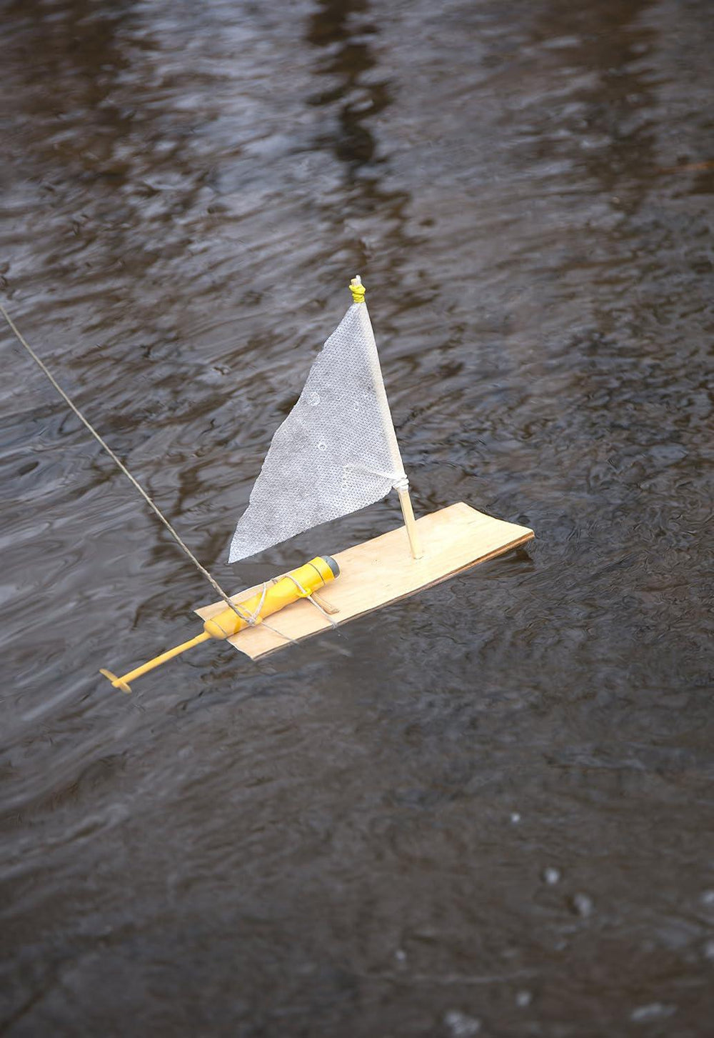 Model sailboat with a yellow body and white sail floating on water