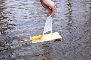 Small sailboat with a yellow motor on a body of water, held by a hand.