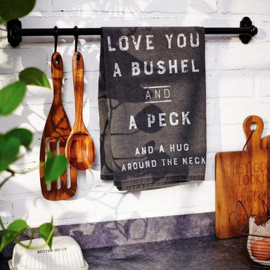 Kitchen towel with text hanging on a rack with wooden utensils and cutting boards.