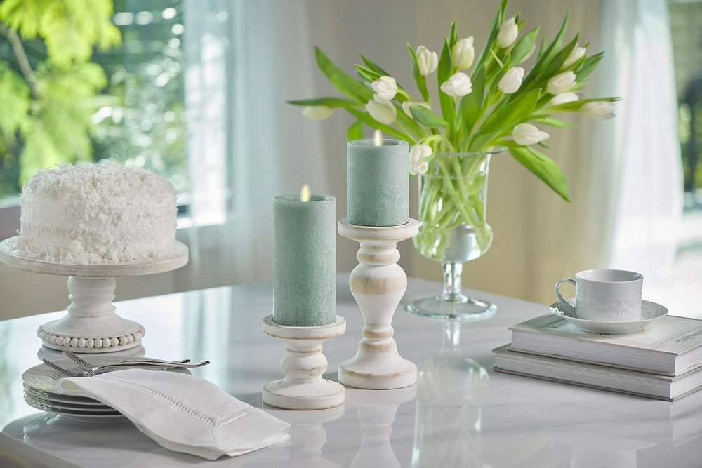 Table setting with a white cake, candles, and a vase of tulips in a bright room. Luminara Iceberg Green Seaglass Flameless LED Pillar – Moving Flame Magic