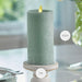 Green candle on a white surface with measurements indicated