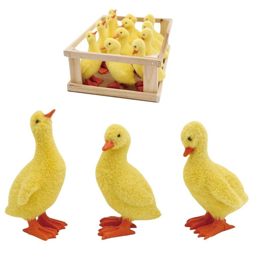 Three yellow duck figurines with red feet in front of a wooden crate filled with more ducklings on a white background.